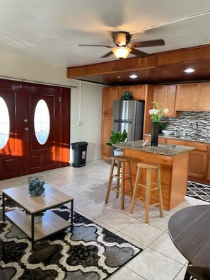 A modern kitchen with wooden cabinets, a stainless steel refrigerator, a built-in island with stools, and a ceiling fan.