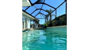 A swimming pool with a glass ceiling structure, clear blue water, and a view of palm trees and a house in the background. - Beautiful Pool Home, 6 Min. to Beaches, Sleeps 8, Great for Families! (Largo)
