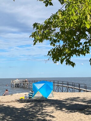 Een strand met een pier, een blauwe tent en een heldere lucht.