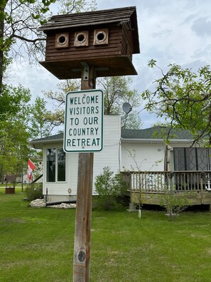 A wooden sign with a birdhouse and a welcome sign for a country retreat.