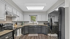 Una cocina moderna con armarios grises oscuros, un refrigerador de acero inoxidable, horno empotrado y encimera de granito.
