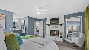 Un dormitorio con una cama grande, una chimenea, un televisor montado encima y un ventilador de techo.