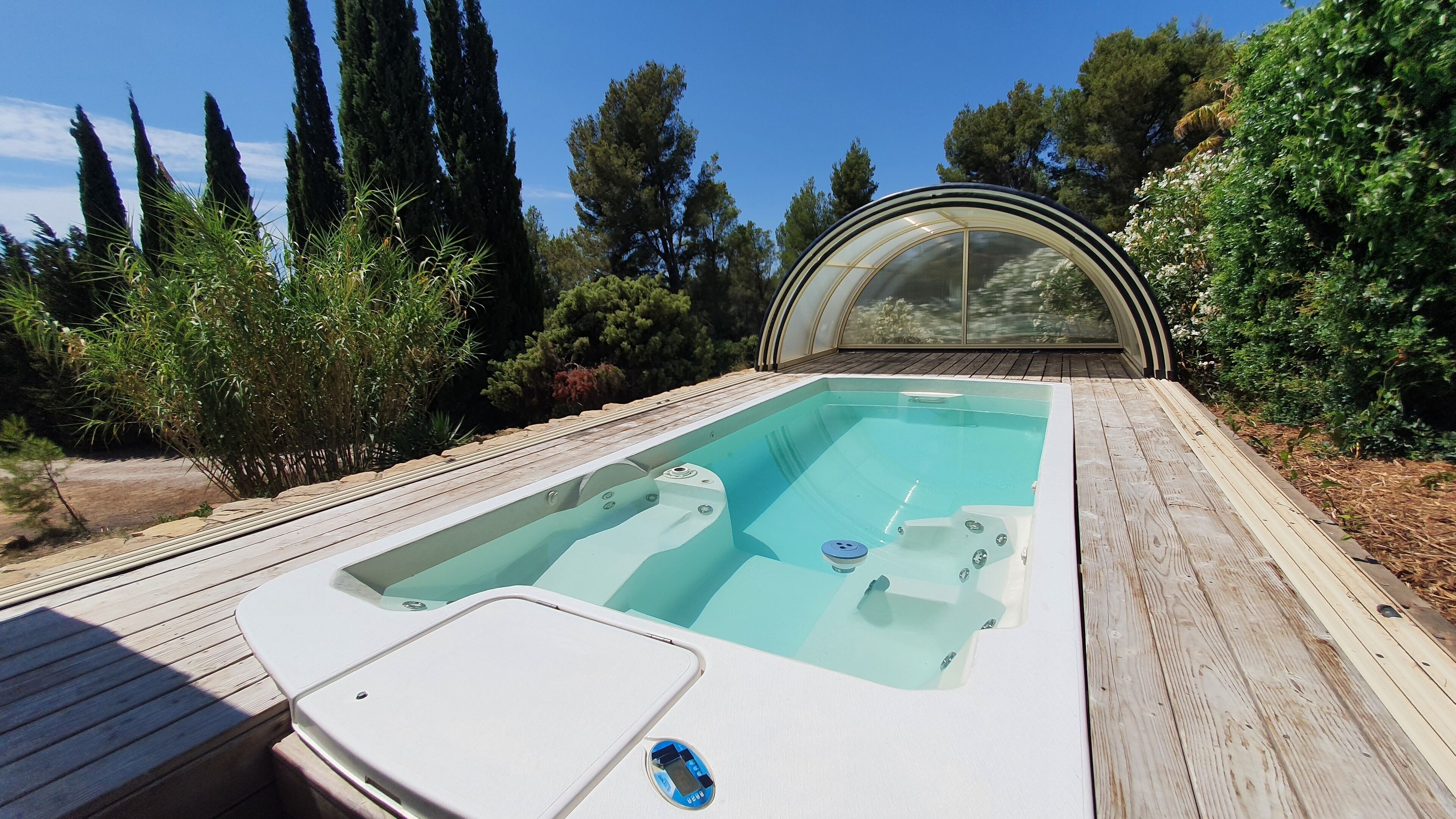 A hot tub with a wooden deck and a glass enclosure, surrounded by greenery.