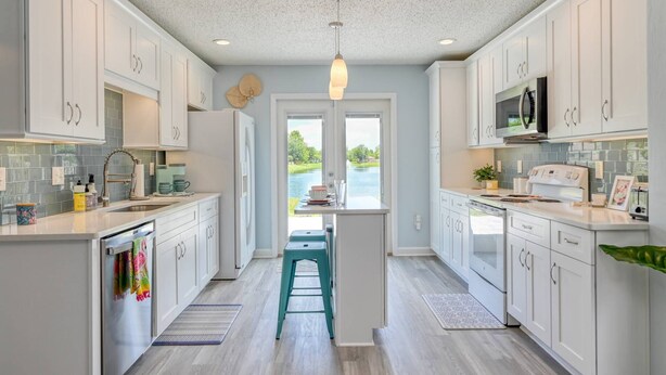 A modern kitchen with white cabinets, a central island, and a view of a lake through the windows. - Wynfield Place (St. Augustine)
