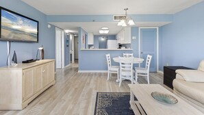 Una sala de estar moderna con comedor, paredes azul claro y cocina al fondo.