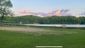 Un parc au bord du lac, équipé d’un filet de volley-ball, de tables de pique-nique et d’un banc.