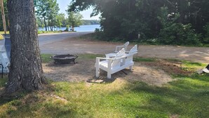 A lakeside seating area with white Adirondack chairs, a fire pit, and a view of the lake. - Cute romantic studio  (Moultonborough)
