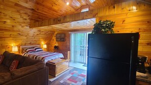 A cozy cabin with a wooden interior, a bed with a striped blanket, a brown leather couch, and a refrigerator. - Cute romantic studio  (Moultonborough)