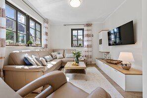 Ein modernes Wohnzimmer mit einem beigefarbenen Sofa, einem Couchtisch und einem an der Wand montierten Flachbildfernseher.