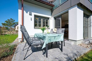 Un espace de restauration en plein air avec une table dressée pour deux personnes, des chaises et une nappe ornée d’un motif de poissons.