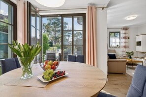Una sala de estar moderna con una mesa redonda de madera, un cuenco de frutas y un florero con plantas verdes.