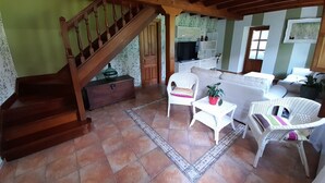 A spacious living area with a wooden staircase, a white sofa, and wicker chairs. - Gestiona2R. House on the coast of Llanes for 8 people (Llanes)