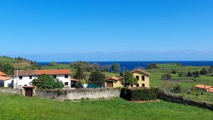 A rural landscape with houses, a stone wall, and a view of the sea. - Gestiona2R. House on the coast of Llanes for 8 people (Llanes)