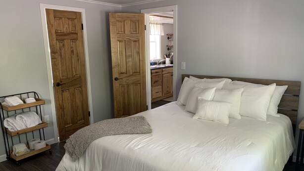 Une chambre avec un grand lit, une armoire en bois et une salle de bain visible à travers une porte ouverte.