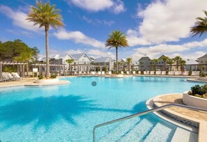 Uma piscina grande com espreguiçadeiras e palmeiras, cercada por edifícios com estilo arquitetônico uniforme.