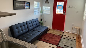 Una sala moderna con un sofá azul oscuro, una encimera de granito con un lavamanos, un cuadro enmarcado en la pared y una puerta roja con ventana.
