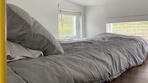 Un dormitorio con cama, ventana con persianas y vista a árboles fuera.