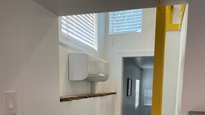 Un pasillo con paredes blancas, piso de madera y una ventana con persianas.