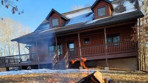 Una baita con un braciere di fronte, circondata dalla neve e da terreno ricoperto di foglie.