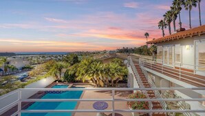 Zona de piscina en la azotea con varias piscinas, palmeras y vistas de la ciudad al atardecer.