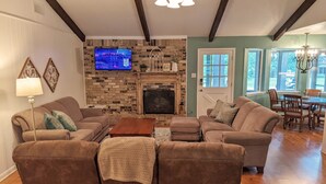 A living room with a fireplace, a television, and a dining area with wooden furniture. - Little Getaway Paradise on the Golf Course w/Resort Amenities! (Holly Lake Ranch)