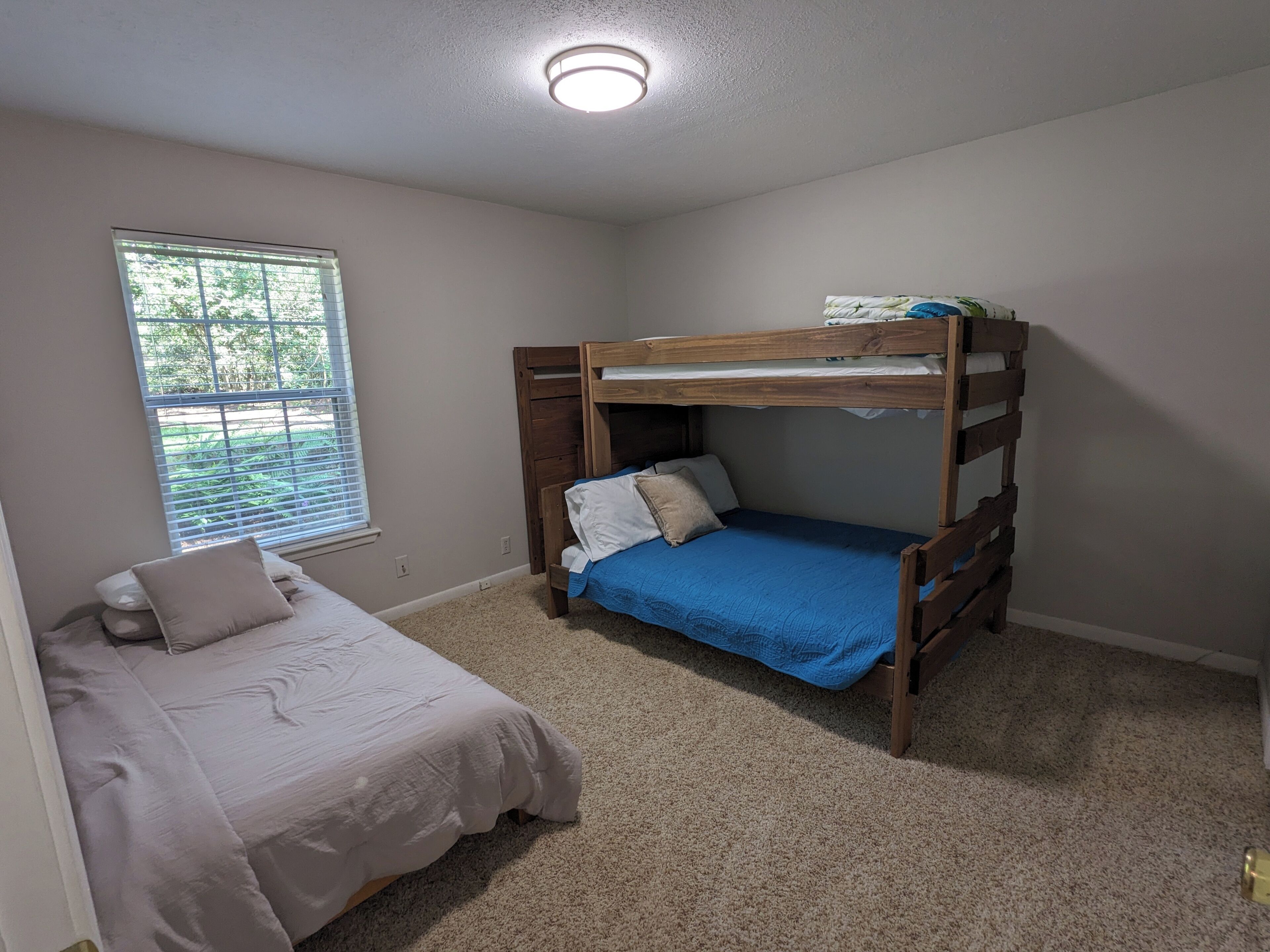 Een slaapkamer met een stapelbed, een enkel bed en een raam met jaloezieën.