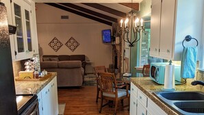 A kitchen with wooden flooring, white cabinets, a dining area with a table and chairs, and a TV mounted on the wall. - Little Getaway Paradise on the Golf Course w/Resort Amenities! (Holly Lake Ranch)