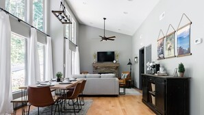 Una sala moderna con chimenea, un comedor con mesa y sillas de madera, y un ventanal con cortinas.
