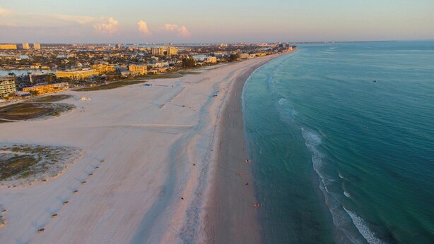 An aerial view of a coastal city with a wide sandy beach, a clear blue ocean, and a dense urban area with buildings in the background. - Madeira Norte - The Perfect Beachfront Escape (Madeira Beach)
