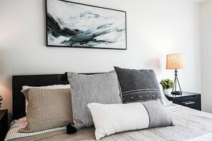 A neatly arranged bedroom with a bed, pillows, a bedside table, a lamp, and a wall-mounted abstract painting. - Modern Microsoft Redmond Campus Condo with Balcony (Bellevue)