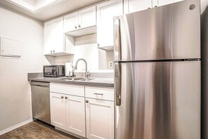 A modern kitchen with white cabinets, a stainless steel refrigerator, a microwave, and a dishwasher. - Modern Microsoft Redmond Campus Condo with Balcony (Bellevue)