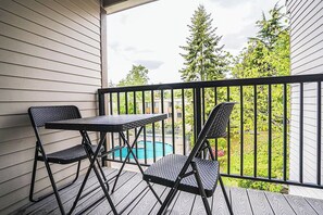 A balcony with a table and two chairs, overlooking a swimming pool and greenery. - Modern Microsoft Redmond Campus Condo with Balcony (Bellevue)