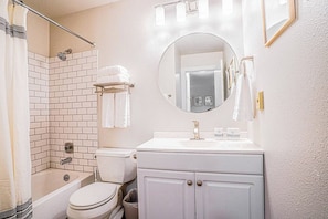 A bathroom with a white bathtub, toilet, and sink, a round mirror, and a shower area. - Modern Microsoft Redmond Campus Condo with Balcony (Bellevue)