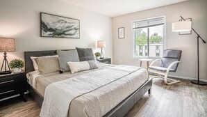 Un dormitorio moderno con una cama grande, lámparas de noche, una silla y una ventana con vistas.