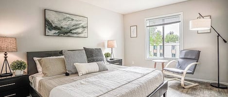 Ein modernes Schlafzimmer mit einem großen Bett, Nachttischlampen, einem Sessel und einem Fenster mit Blick.