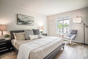 A modern bedroom with a large bed, bedside lamps, a chair, and a window with a view. - Modern Microsoft Redmond Campus Condo with Balcony (Bellevue)