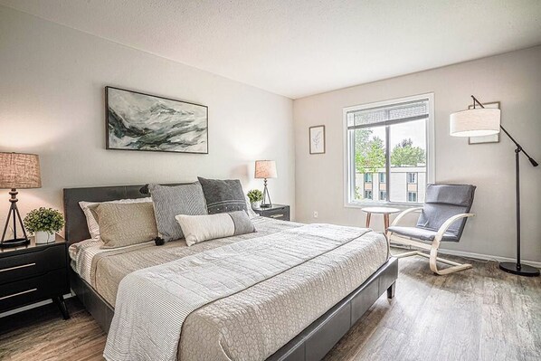 Une chambre moderne avec un grand lit, des lampes de chevet, un fauteuil et une fenêtre donnant sur un beau paysage.