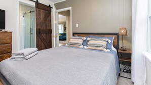 Una camera da letto con un letto grande, un comò in legno, una porta scorrevole in stile rustico e una lampada da comodino.