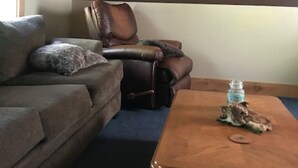 Un salon avec un canapé en cuir marron, un fauteuil inclinable, une table basse et une tête de cerf accrochée au mur.