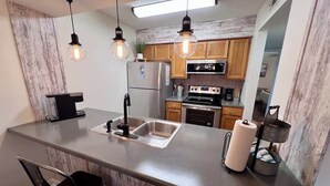 Une cuisine moderne dotée d’un îlot central, d’appareils électroménagers en acier inoxydable et de luminaires suspendus.