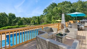 A poolside area with a wooden deck, wicker furniture, and a hot tub.