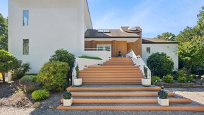 A modern house with a staircase leading to the entrance, surrounded by well-maintained gardens.