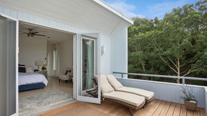 A balcony with two lounge chairs, a wooden deck, and a view of trees.