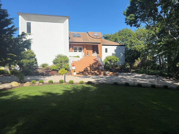 A modern two-story house with a white exterior, a wooden staircase, and a well-maintained garden. - Private 2.1 acre gated home with heated pool and tennis & pickleball court (Southampton)
