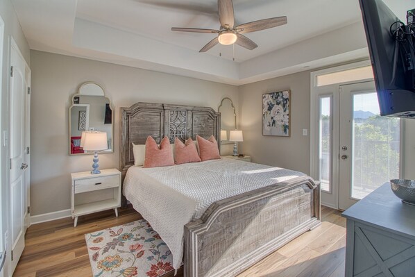 Une chambre à coucher avec une tête de lit en bois, deux tables de chevet avec des lampes, un tapis à motifs floraux et un ventilateur de plafond.