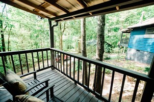 A wooden deck with a railing, a bench, and a view of a forested area and a blue building.