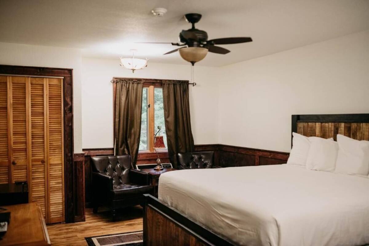 Un dormitorio con cama, escritorio, silla, ventilador de techo y ventana con cortinas.