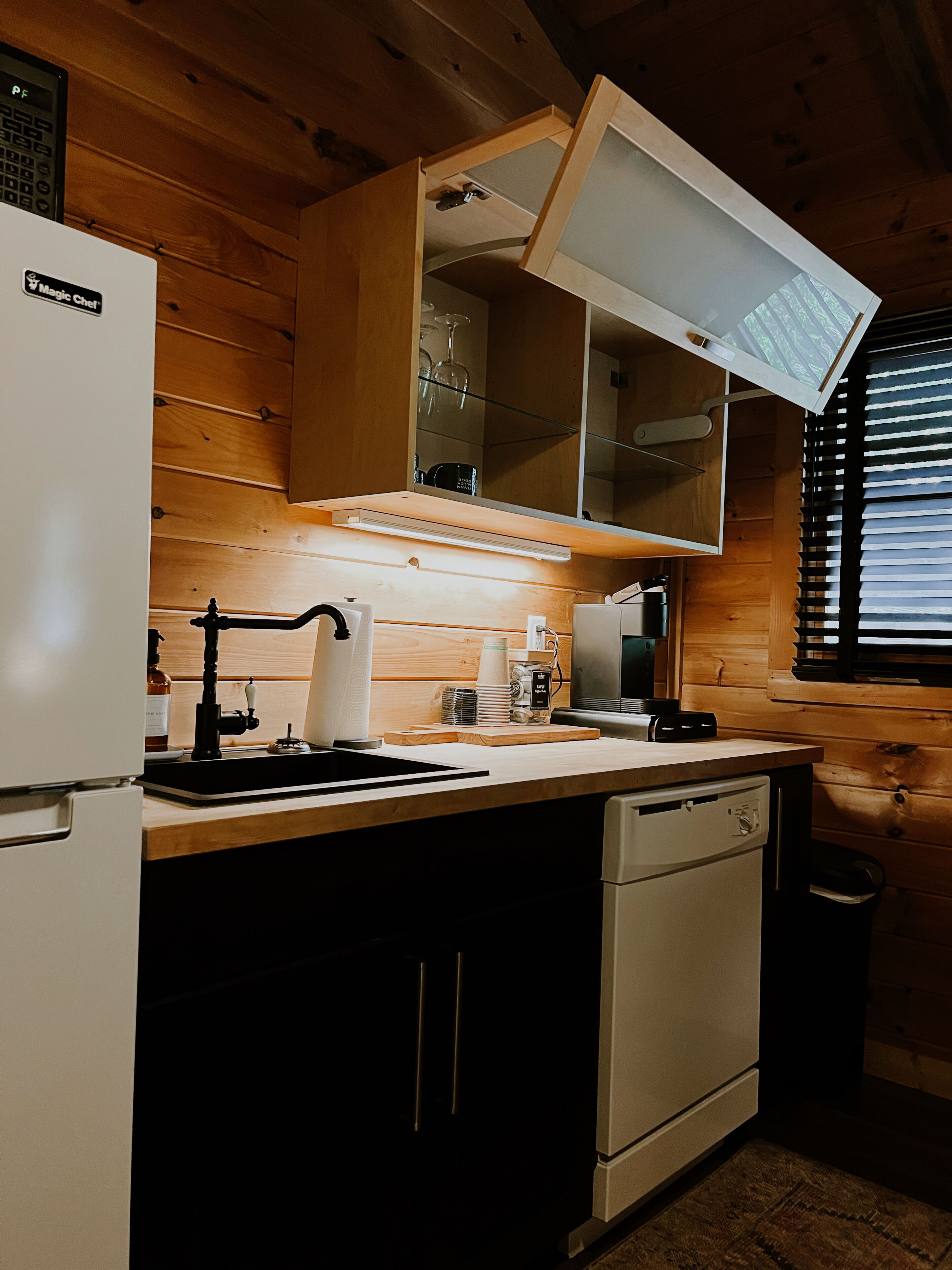 A compact kitchen with wooden walls, a white refrigerator, a sink, and a dishwasher.