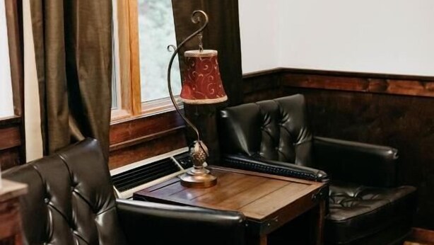 A room with a wooden floor, dark brown leather sofa, a small wooden table, and a window with curtains. - Sylvan Valley Lodge & Cellars (Sautee Nacoochee)