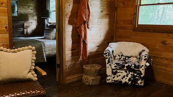 A cozy cabin interior with a bed, a wooden bench, a patterned rug, and a cow-print armchair.